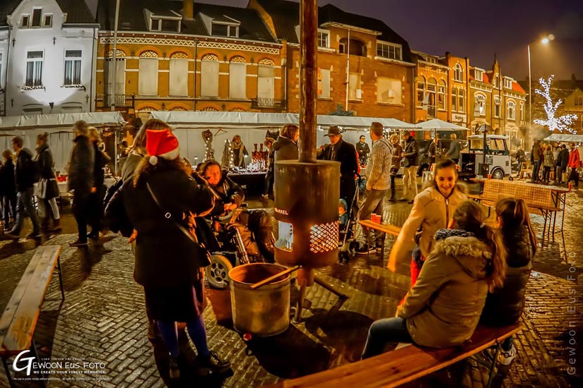 Bezoekers verzameld op bankjes rond een brandende Burning Barrel op een avondmarkt