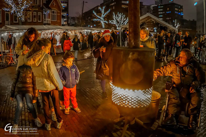 Een gezin verzameld rond een brandende Burning Barrel op een wintermarkt