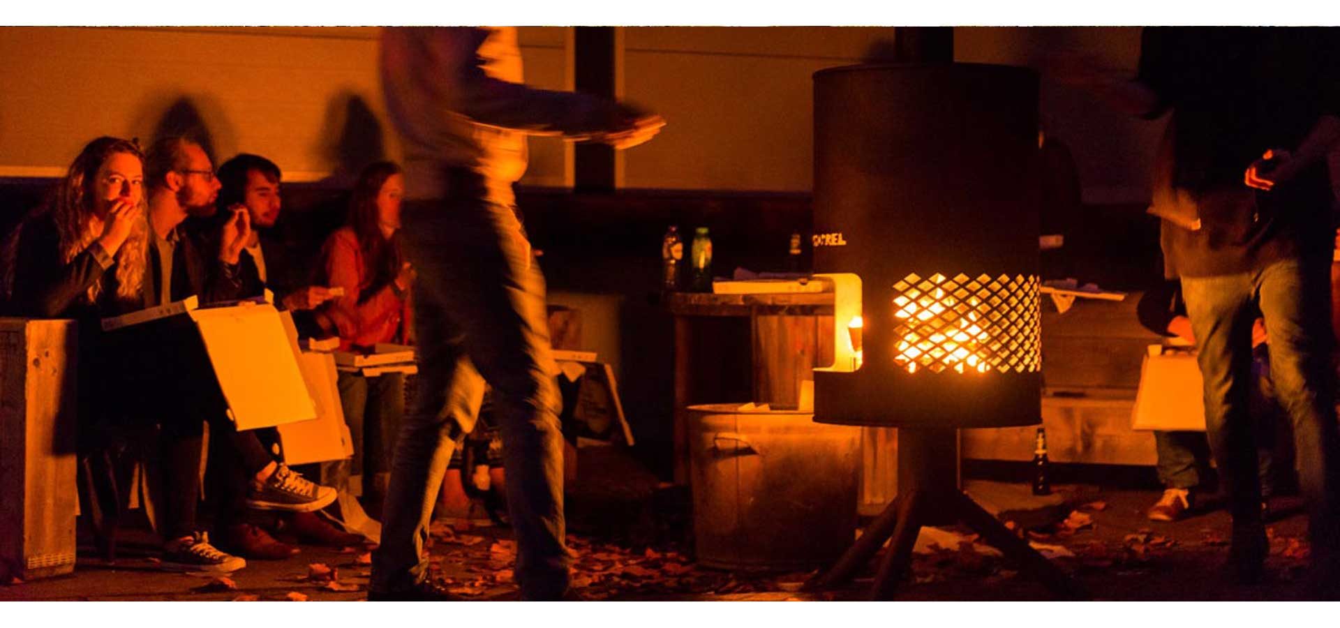 Een groep mensen verzameld rond een brandende Burning Barrel tijdens een avondevenement